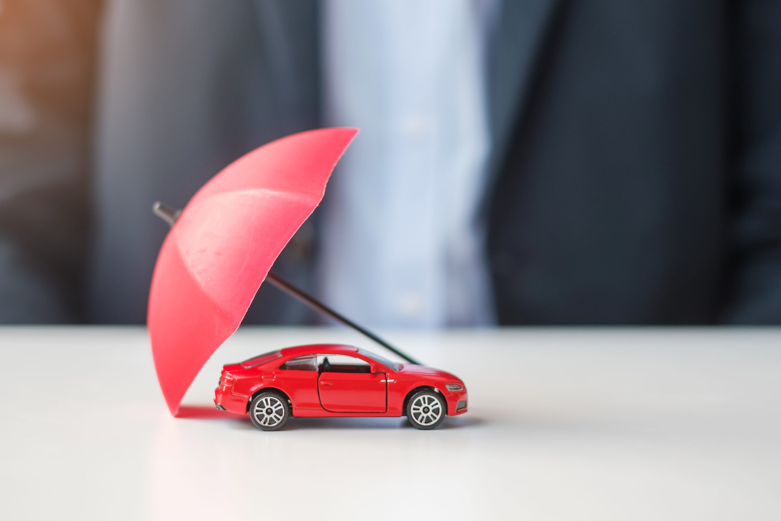 Businessman hand holding umbrella and cover red car toy on tabl Businessman hand holding umbrella and cover red car toy on table. Car insurance, warranty, repair, Financial, banking and money concept